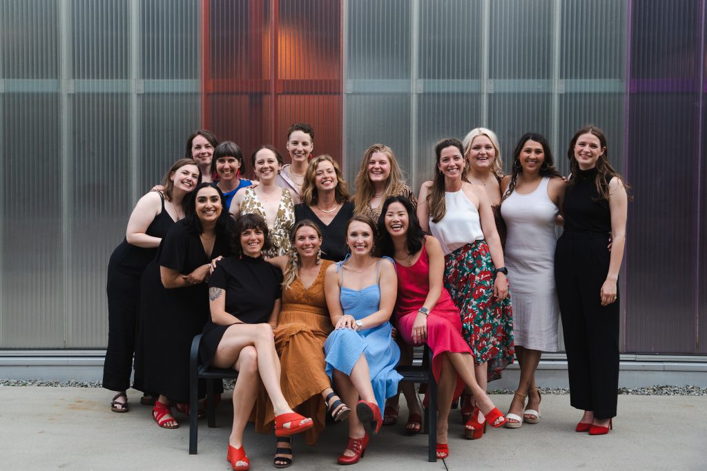 2023 UBC Midwifery Program Graduates celebrating their achievement, a group of women sitting and standing together, smiling with joy and pride.