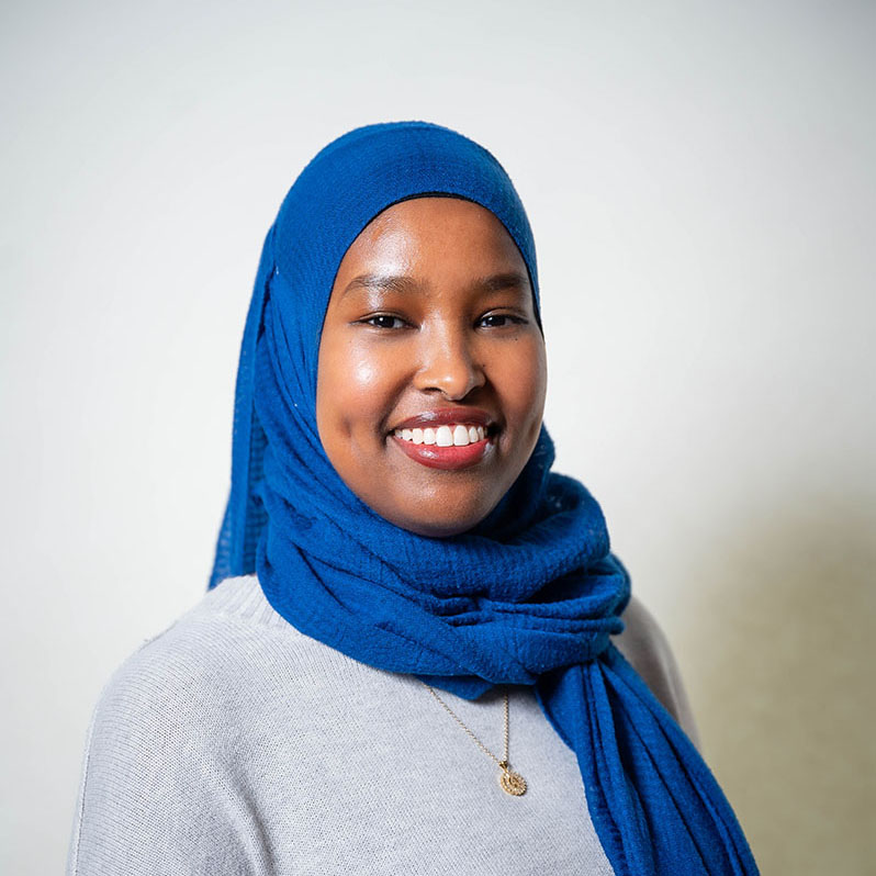 Young woman wearing a blue hijab and smiling.