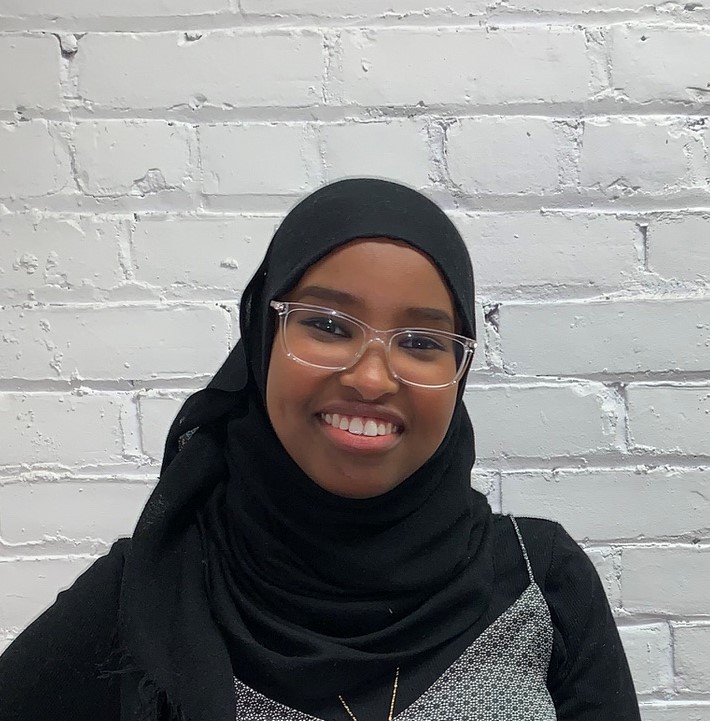 A joyful woman wearing glasses and a Hijab, smiling warmly.