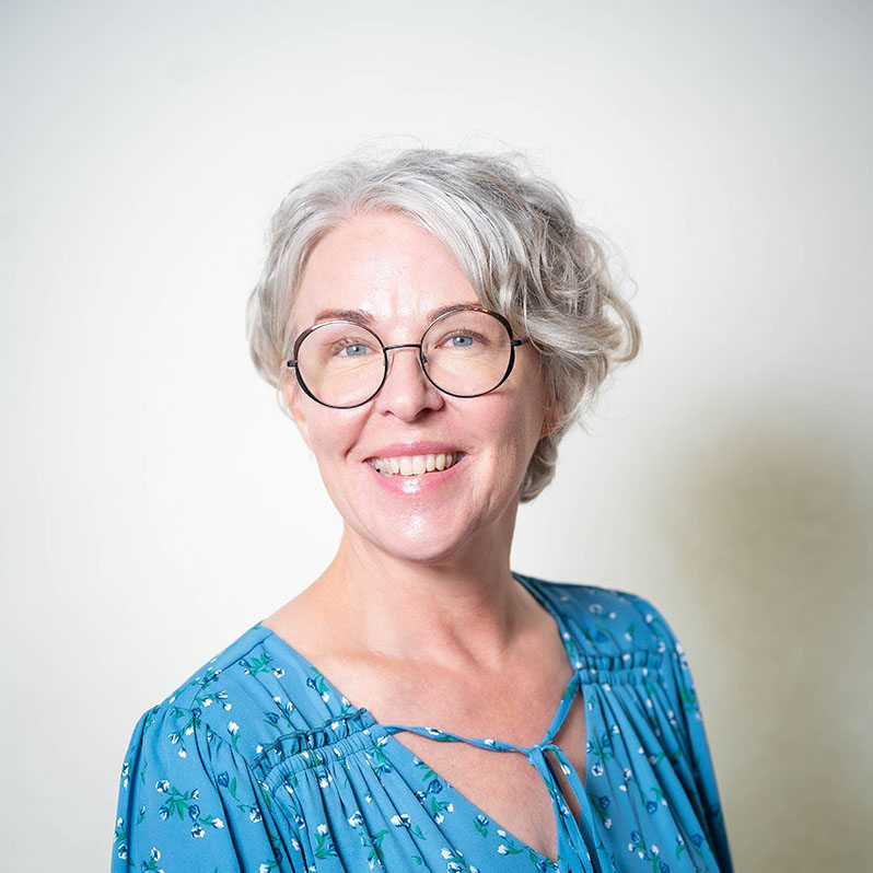 Brightly smiling woman with round glasses and short wavy silver hair.
